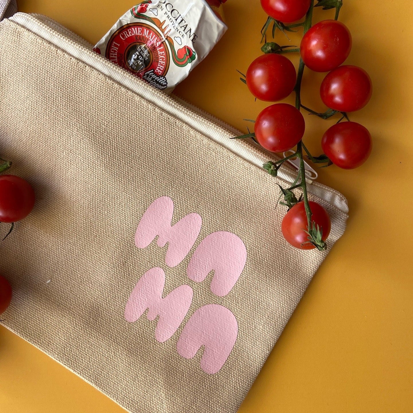 A beige multifunctional bag with the word 'MAMA' written in pink on the front, displayed alongside some cherry tomatoes.