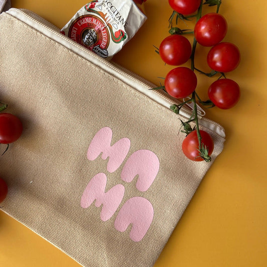 A beige multifunctional bag with the word 'MAMA' written in pink on the front, displayed alongside some cherry tomatoes.